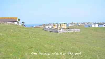 a field of grass with houses on a hill at G22 Happy Days, Riviere Towans in Hayle