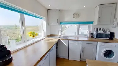 a kitchen with white cabinets and a sink and a window at G22 Happy Days, Riviere Towans in Hayle