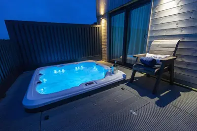 a hot tub on a balcony with a chair and a bench at Dahlia in Redruth