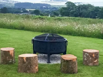 a fire pit in a field with three logs at Scenic Bay in Penzance