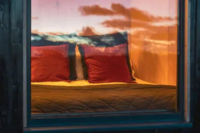 a bed with two red pillows is seen through a window at Cabins at Bogee Farm in Saint Ervan