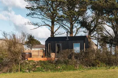 a black house in a field with trees at Cabins at Bogee Farm in Saint Ervan