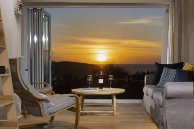 a living room with a table and a window with a sunset at Sunset Sands in St Merryn