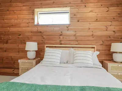 a bedroom with wooden walls and a bed with two lamps at Teach Tra East in Perranporth