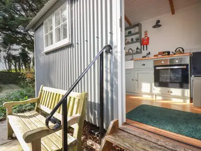 a wooden bench sitting on a porch next to a kitchen at Hilbre Shepherd Hut in Padstow