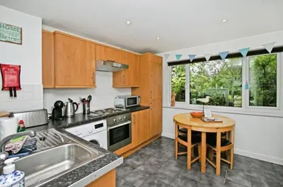 a kitchen with wooden cabinets and a small table at Atlantic Reach – Cozy 2-Bed with Parking in Newquay
