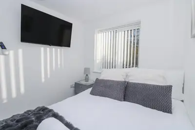 a white bedroom with a bed with a flat screen tv at Cosy Retreat in Camborne