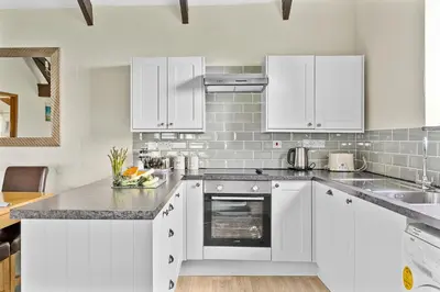 a white kitchen with white cabinets and a sink at Fuchsia Cottage in Saint Endellion