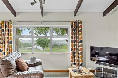 a living room with a couch and a large window at Fuchsia Cottage in Saint Endellion