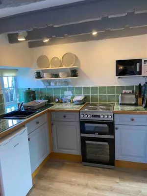 a kitchen with white cabinets and a stove top oven at Buntings Cottage at Trenale Court Cottages in Tintagel
