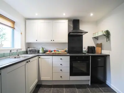 a kitchen with white cabinets and a black stove at Bramble Cottage in Saint Columb Minor