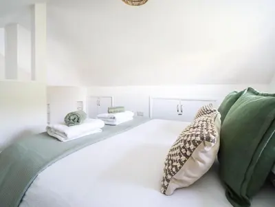a white bedroom with a bed with green pillows at Bramble Cottage in Saint Columb Minor