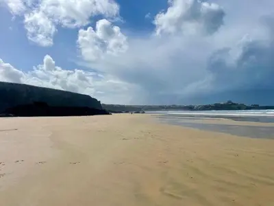 a sandy beach with a cloudy sky and the ocean at Bramble Cottage in Saint Columb Minor