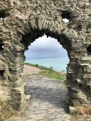 an arch in a stone wall near the ocean at Wren Cottage at Trenale Court Cottages in Tintagel