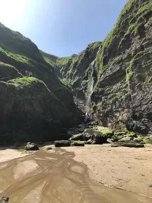 a waterfall in a mountain with a sandy beach at Plover Cottage at Trenale Court Cottages in Tintagel