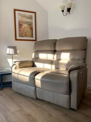 a leather couch in a living room with a lamp at Plover Cottage at Trenale Court Cottages in Tintagel