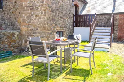 a table and chairs in a yard next to a building at Finest Retreats - Fields Barn in Widemouth Bay