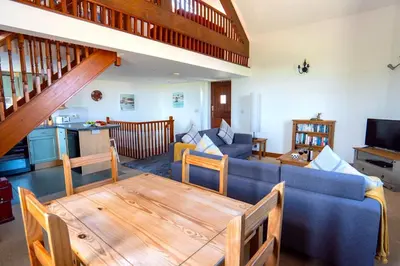 a living room with a blue couch and a wooden table at Finest Retreats - Fields Barn in Widemouth Bay
