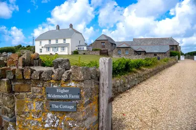 a stone wall with a sign in front of a house at Finest Retreats - Rosemary Cottage in Widemouth Bay