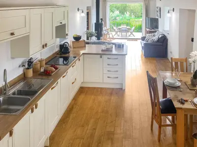 a kitchen with white cabinets and a wooden floor at Swallows in Porthscatho