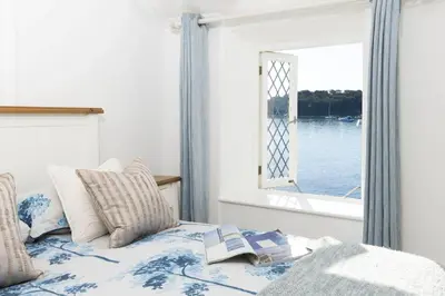 a bed with a book on it with a window at Mariners Cottage in Saint Mawes