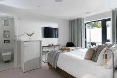 a white bedroom with a bed and a tv on the wall at Fistral house Beachfront Bliss in Crantock