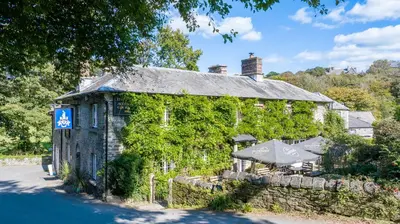 a building covered in ivy with a table and an umbrella at The Falcon Inn in Saint Mawgan