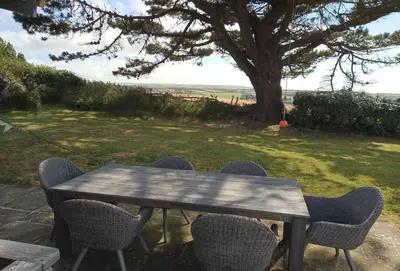 a picnic table with chairs and a tree in a field at Little Penrose Cottage in Bude