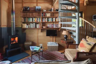 a living room with a fireplace and a book shelf at The Beech Hut, Wood Fired Hot Tub, St Kew Escapes in Saint Kew