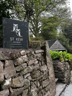 a sign for the st kew garden with a stone wall at The Beech Hut, Wood Fired Hot Tub, St Kew Escapes in Saint Kew