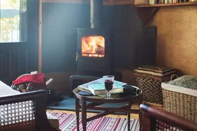 a glass of wine on a table in a room with a fireplace at The Beech Hut, Wood Fired Hot Tub, St Kew Escapes in Saint Kew