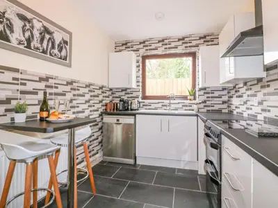 a kitchen with white cabinets and a table with chairs at Camellia Cottage in Bodmin