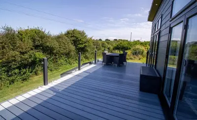 a wooden deck with a table on the side of a building at Teal Lodge Cornwall - hot tub, indoor pool, near Perranporth in Cubert
