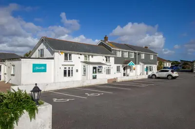 a white building with a car parked in a parking lot at Teal Lodge Cornwall - hot tub, indoor pool, near Perranporth in Cubert