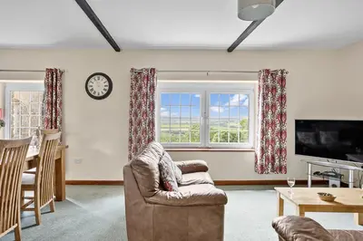 a living room with a chair and a tv and two windows at Cherry Cottage in Saint Endellion