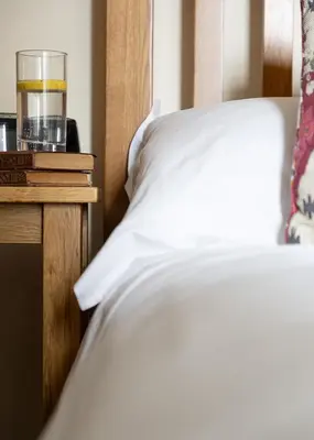 a bed with a glass of water on a table at Cherry Cottage in Saint Endellion