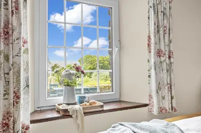 a window with a vase of flowers on a shelf at Cherry Cottage in Saint Endellion