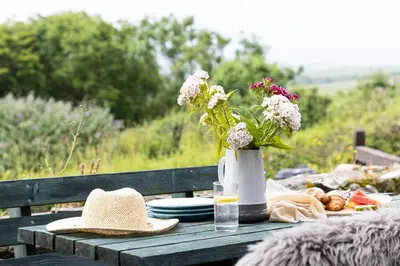 a picnic table with a vase of flowers and a hat at Cherry Cottage in Saint Endellion