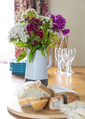 a vase with flowers and bread on a table at Cherry Cottage in Saint Endellion