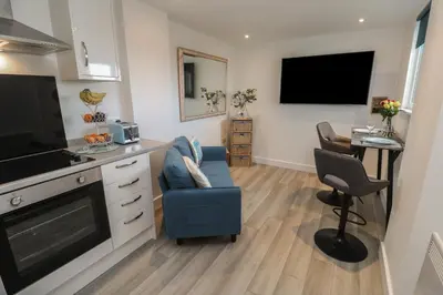 a living room with a blue couch and a kitchen at Sea Whispers in Marazion