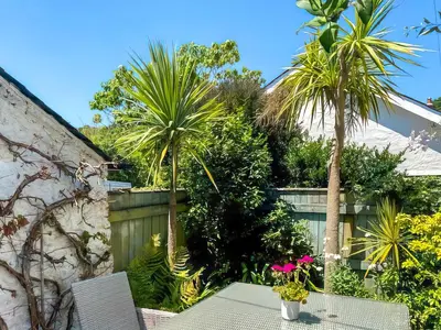 a table and chairs in a garden with palm trees at Shearwaters in Truro