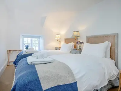 two beds in a bedroom with white and blue sheets at Cellars Cottage in Porthscatho
