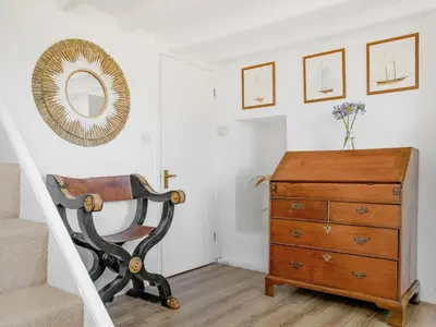 a room with a chair and a dresser and a mirror at Cellars Cottage in Porthscatho
