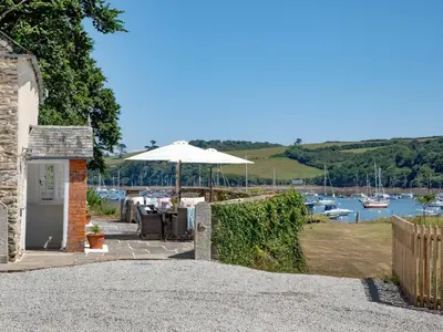 a patio with an umbrella and boats in the water at Cellars Cottage in Porthscatho