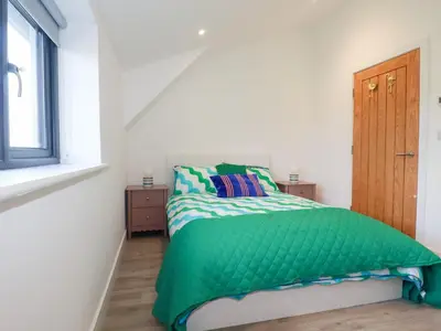 a bedroom with a bed with a green comforter and a window at Barn 5 in St Austell