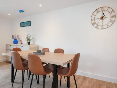 a dining room table with chairs and a clock on the wall at Barn 5 in St Austell