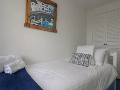 a white bed in a room with a picture on the wall at Driftwood Cottage in St Austell