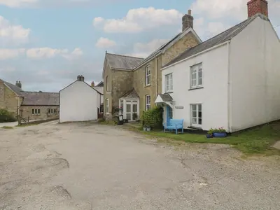 a large white house with a blue bench in front of it at Driftwood Cottage in St Austell