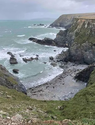 a beach with rocks and the ocean on a hill at Cornwall Shepherds Hut - Hot Tub & Cosy Log Burner in Saint Day