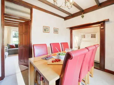 a dining room with a wooden table and red chairs at Foxglove Cottage in Liskeard